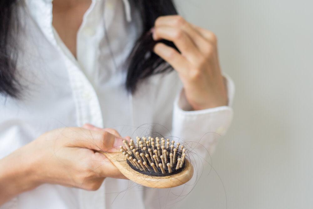 Woman holding a hair brush with lots of loose hair tangled in the bristles.