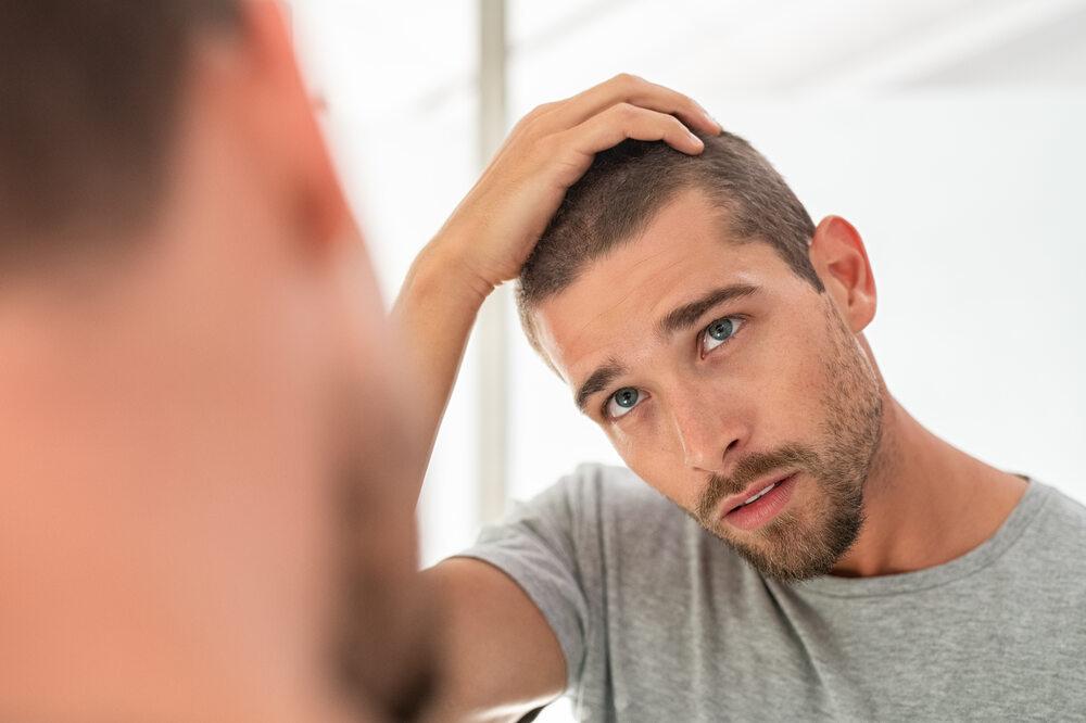 A man looking in a mirror and touching his hair