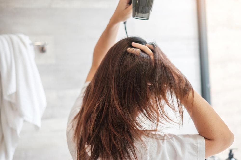 Woman blow-drying her hair to boost volume for hair and prevent flat hair after washing